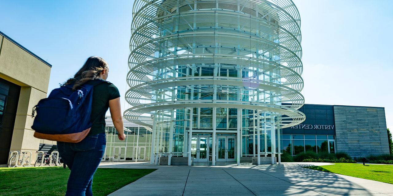 A student wearing a backpack walks toward the entrance of the Visitor Center and University Bookstore.